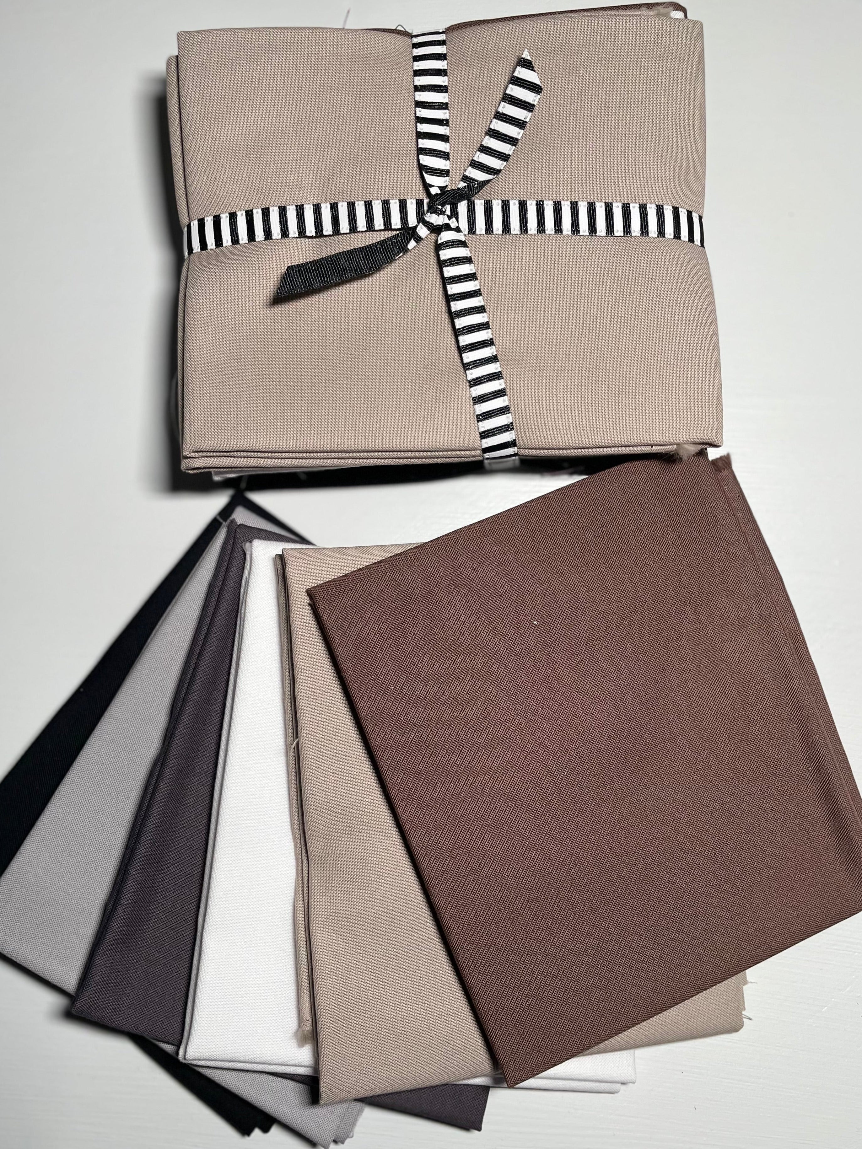Collection of fabric swatches in neutral colors with a striped ribbon on a white background