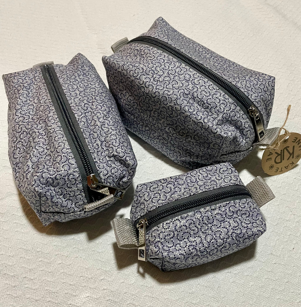 Three gray floral-patterned pouches with zippers on a light beige background