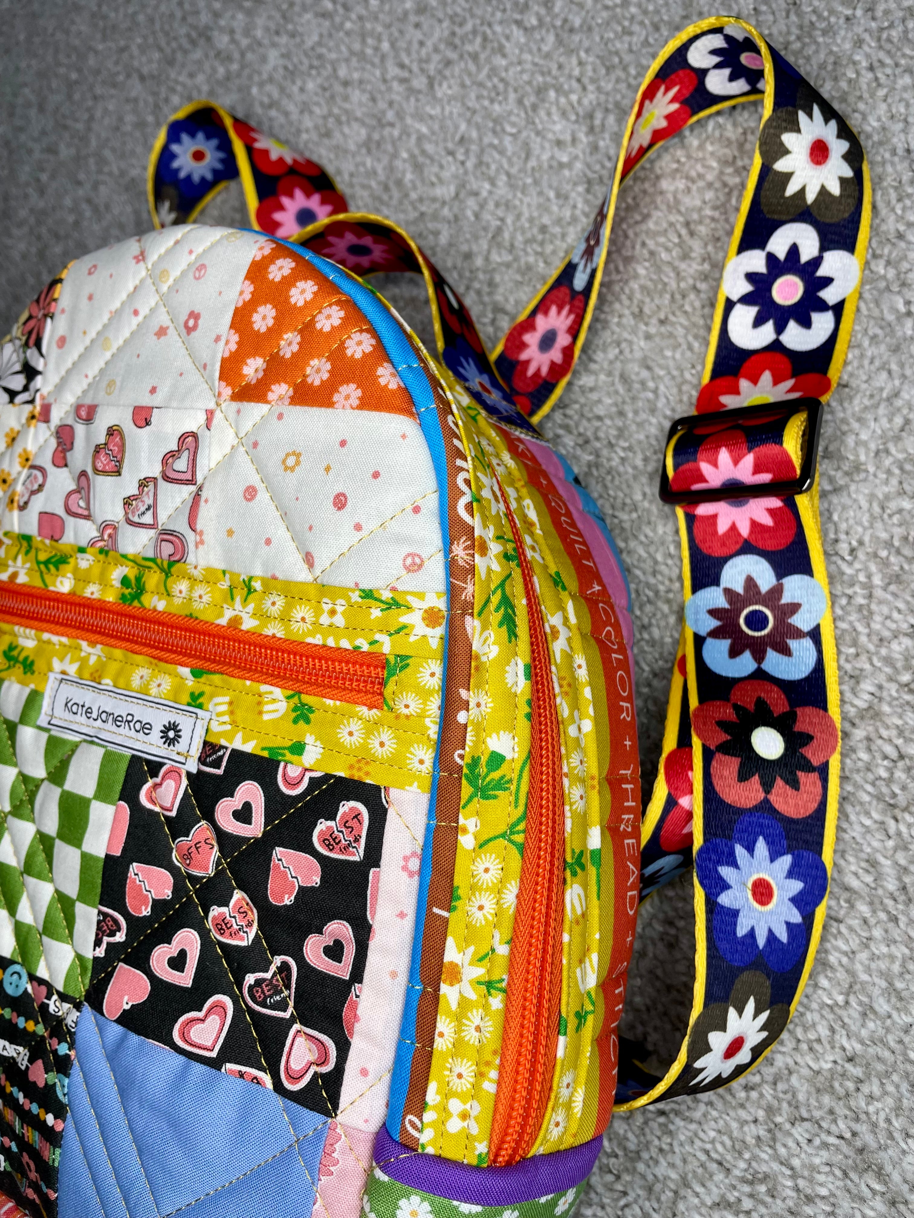 Colorful quilted backpack with patterned strap on a gray surface