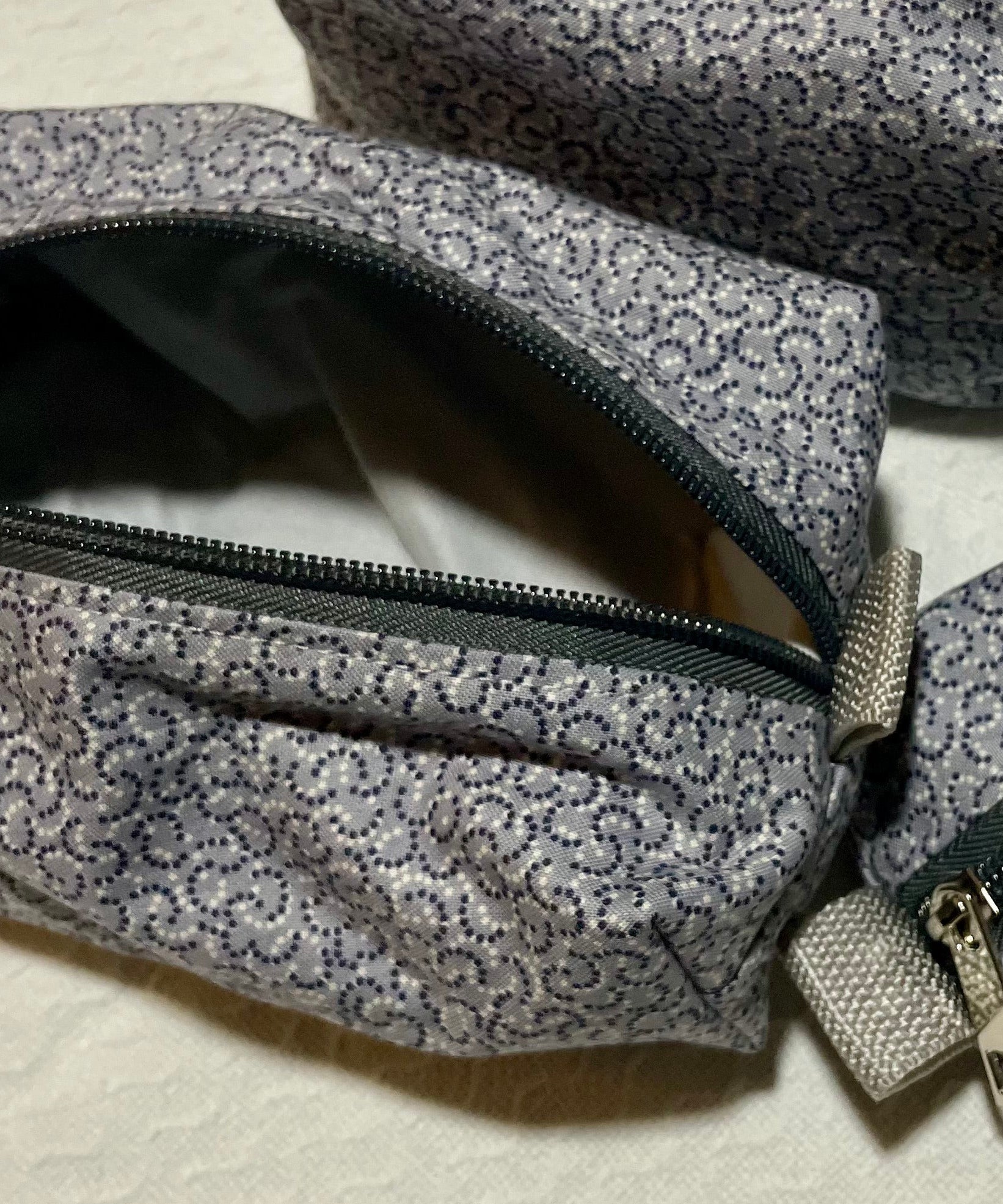 Three gray floral-patterned zippered pouches on a beige surface