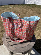 Red floral-patterned sun hat with blue interior on a wooden chair outdoors.
