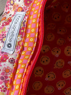 Floral-patterned makeup bag with a visible brand label on a wooden surface.