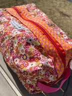 Floral-patterned bag with a pink handle on a wooden surface
