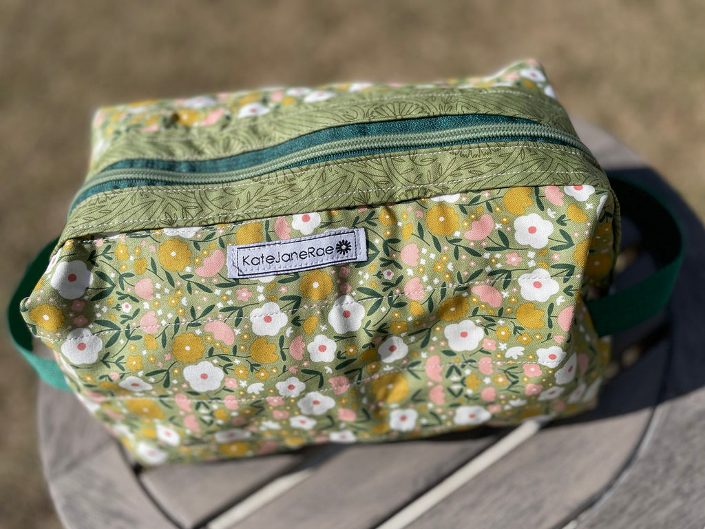 Floral-patterned toiletry bag with a visible brand label on a blurred background