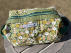 Floral-patterned toiletry bag with a visible brand label on a blurred background