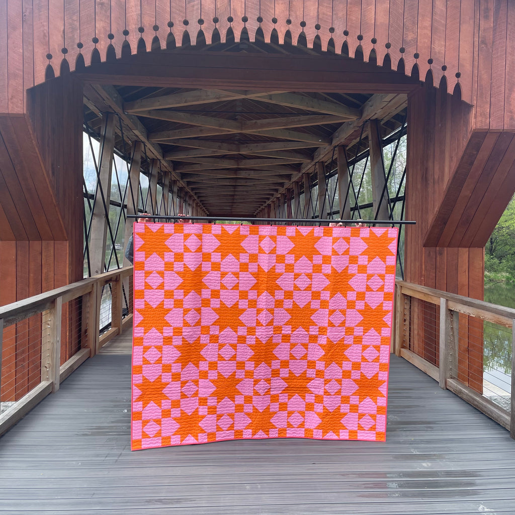 Quilt with pink and orange pattern displayed on a wooden bridge