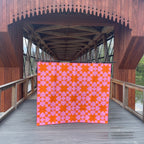 Quilt with pink and orange pattern displayed on a wooden bridge