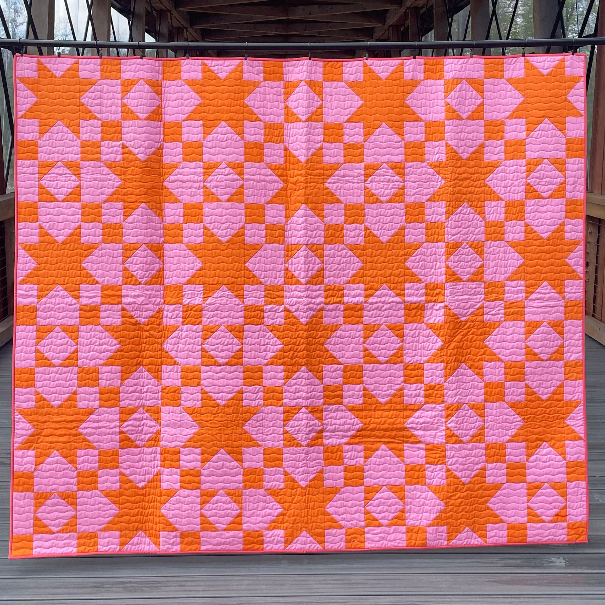 Quilt with pink and orange geometric pattern on a wooden deck