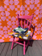 Pink chair with colorful bags on a pink and orange quilt