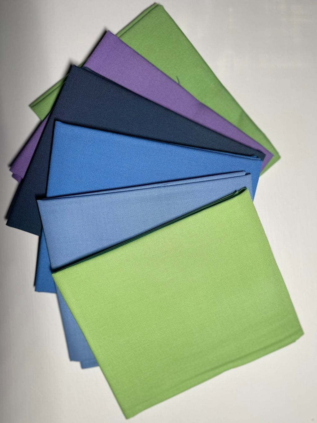 Stack of green, purple, and blue fabric on a white background
