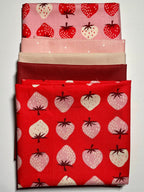 Strawberry & pink/red fabric bundle on white table.