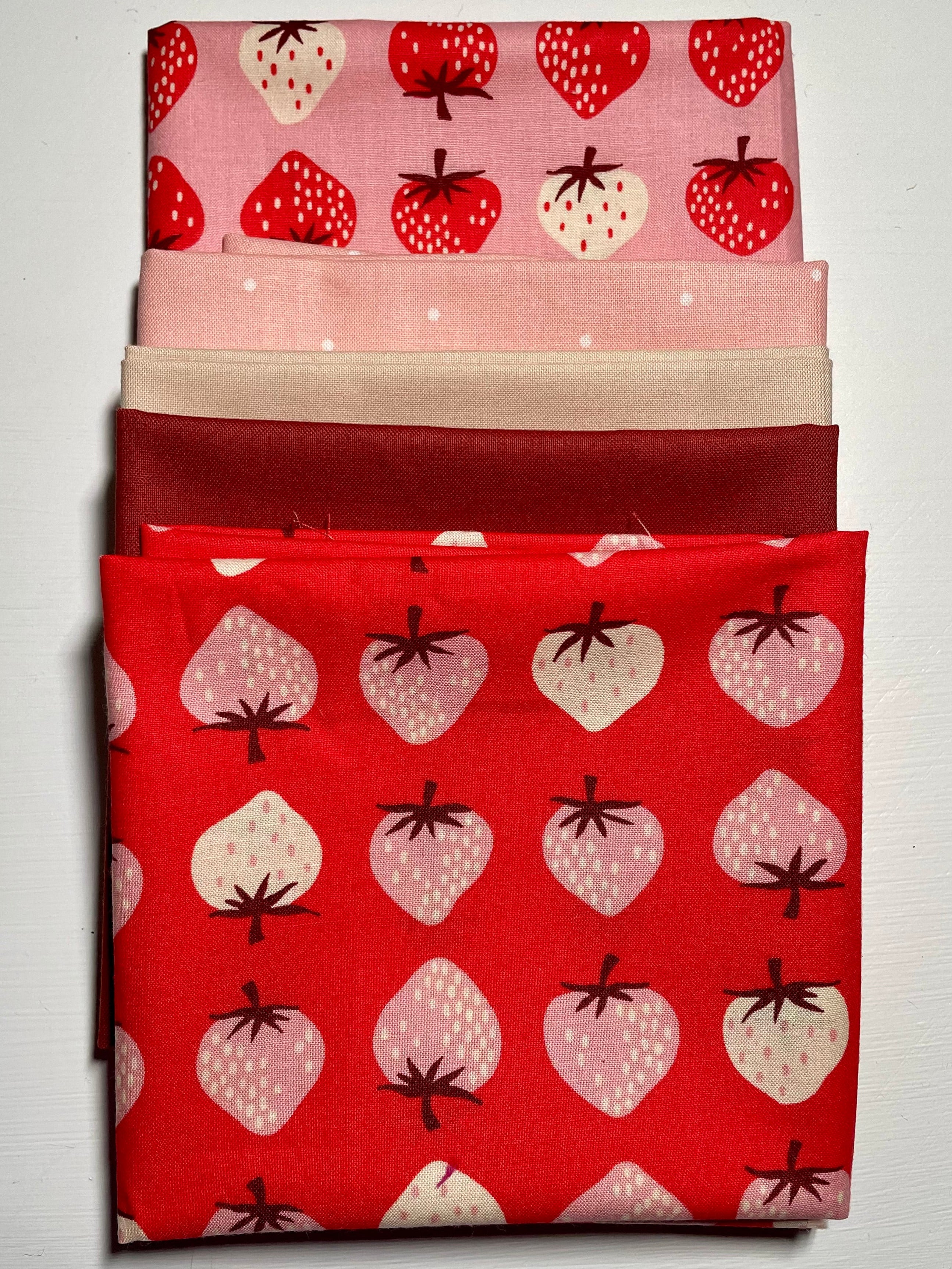 Strawberry & pink/red fabric bundle on white table.
