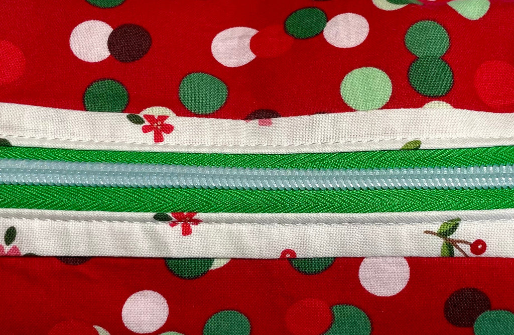 Red polka dot pouch with green and white zipper on a light gray background