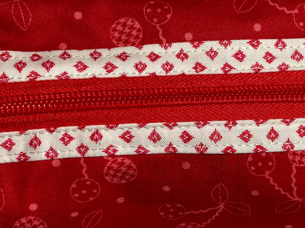 Red fabric pouch with white zipper and pattern on a light gray background
