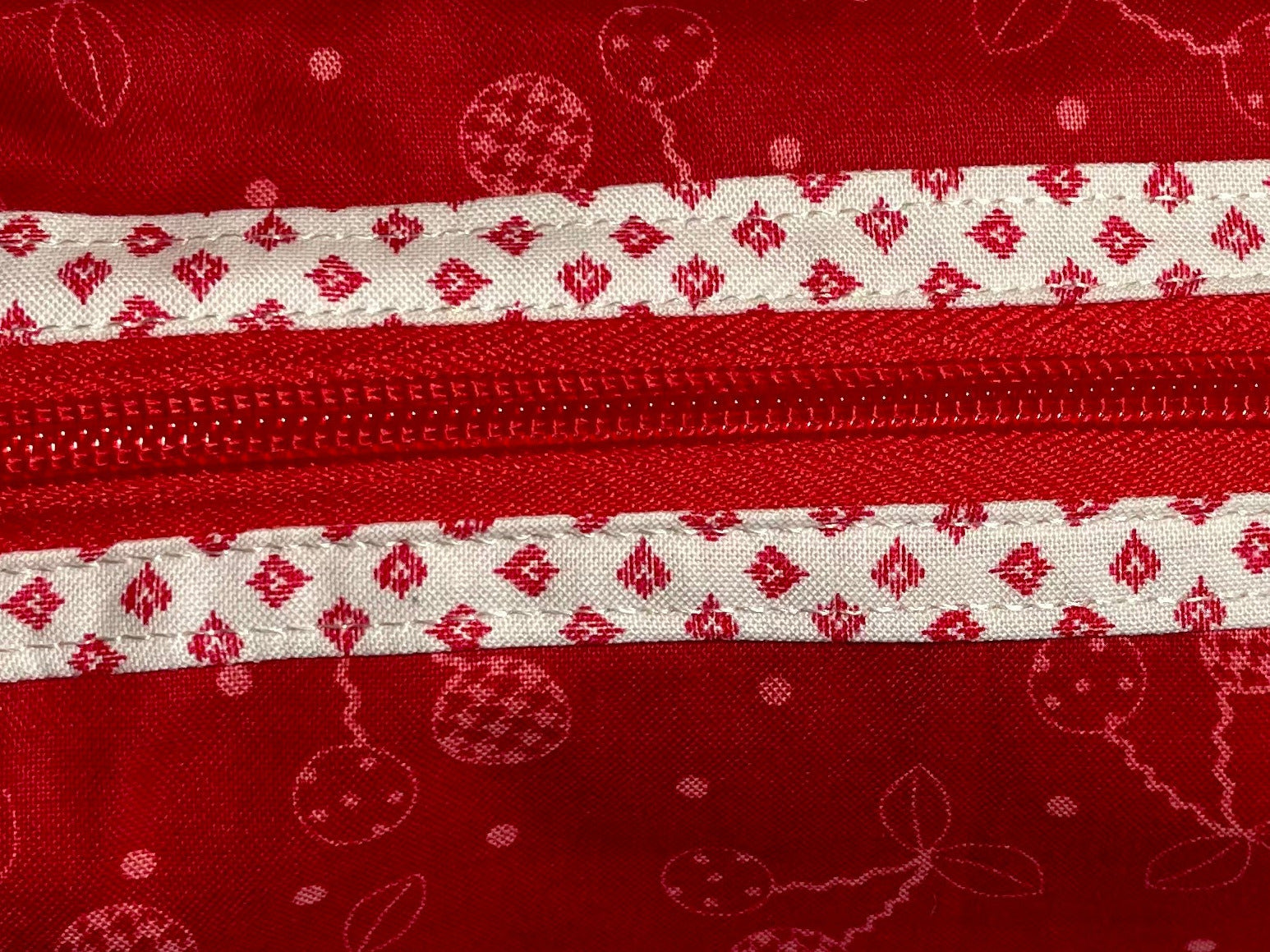 Red fabric pouch with white zipper and pattern on a light gray background