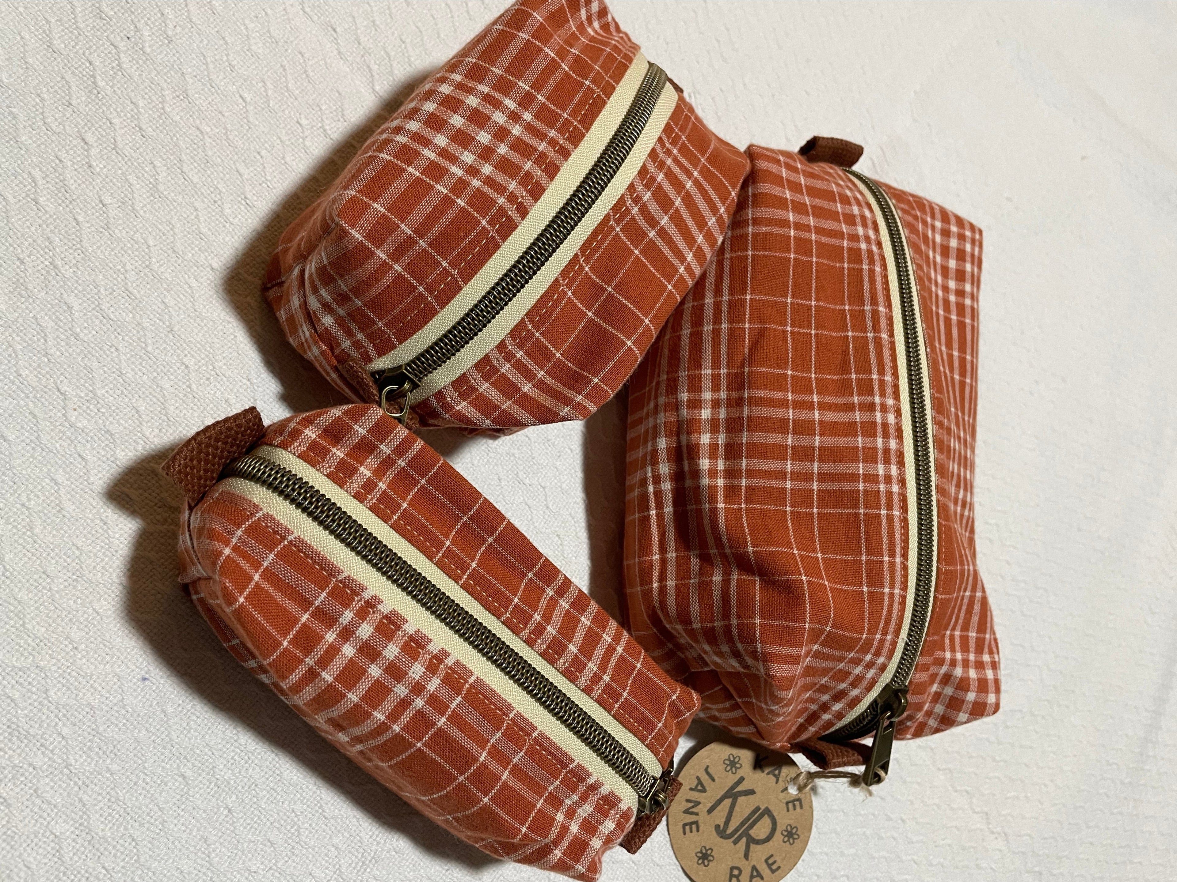 Three brown plaid pouches with zippers on a white background