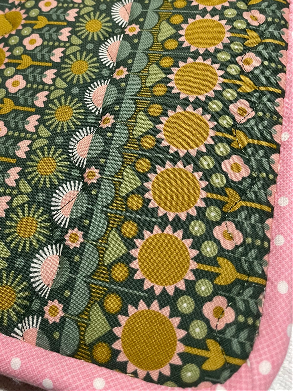 Fabric with sunflower pattern on a green background, bordered by pink fabric.
