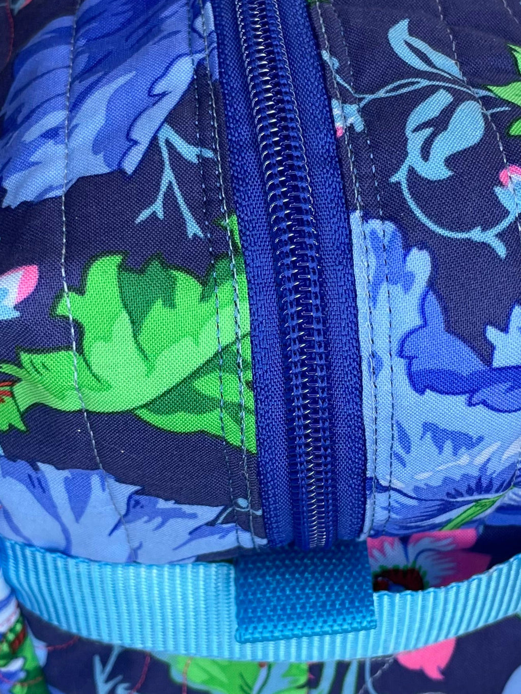 Floral-patterned pencil case with a blue zipper on a beige carpet