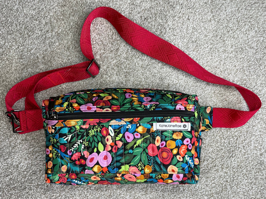 Floral patterned waist bag with a red strap on a gray surface
