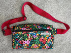 Floral patterned waist bag with a red strap on a gray surface