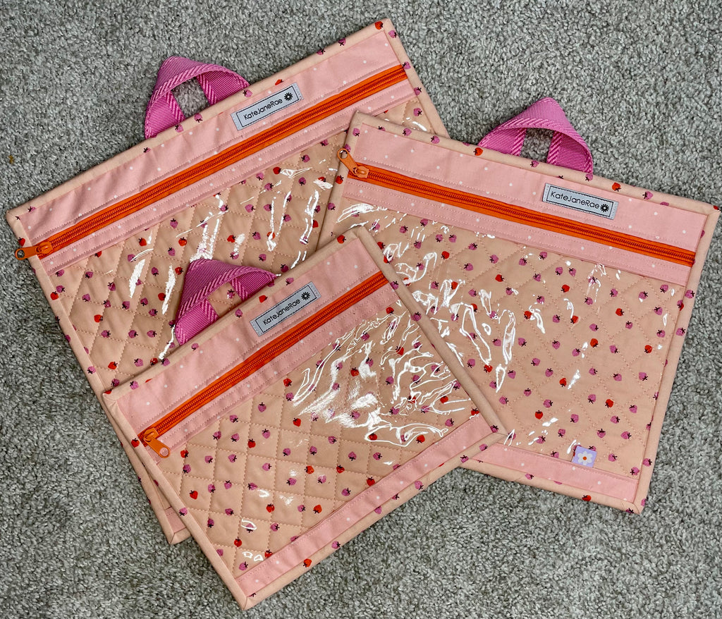 Set of three pink pouches with clear front pockets on a gray surface