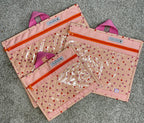 Set of three pink pouches with clear front pockets on a gray surface