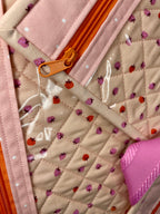 Close-up of a quilted fabric with ladybug pattern and orange zipper.