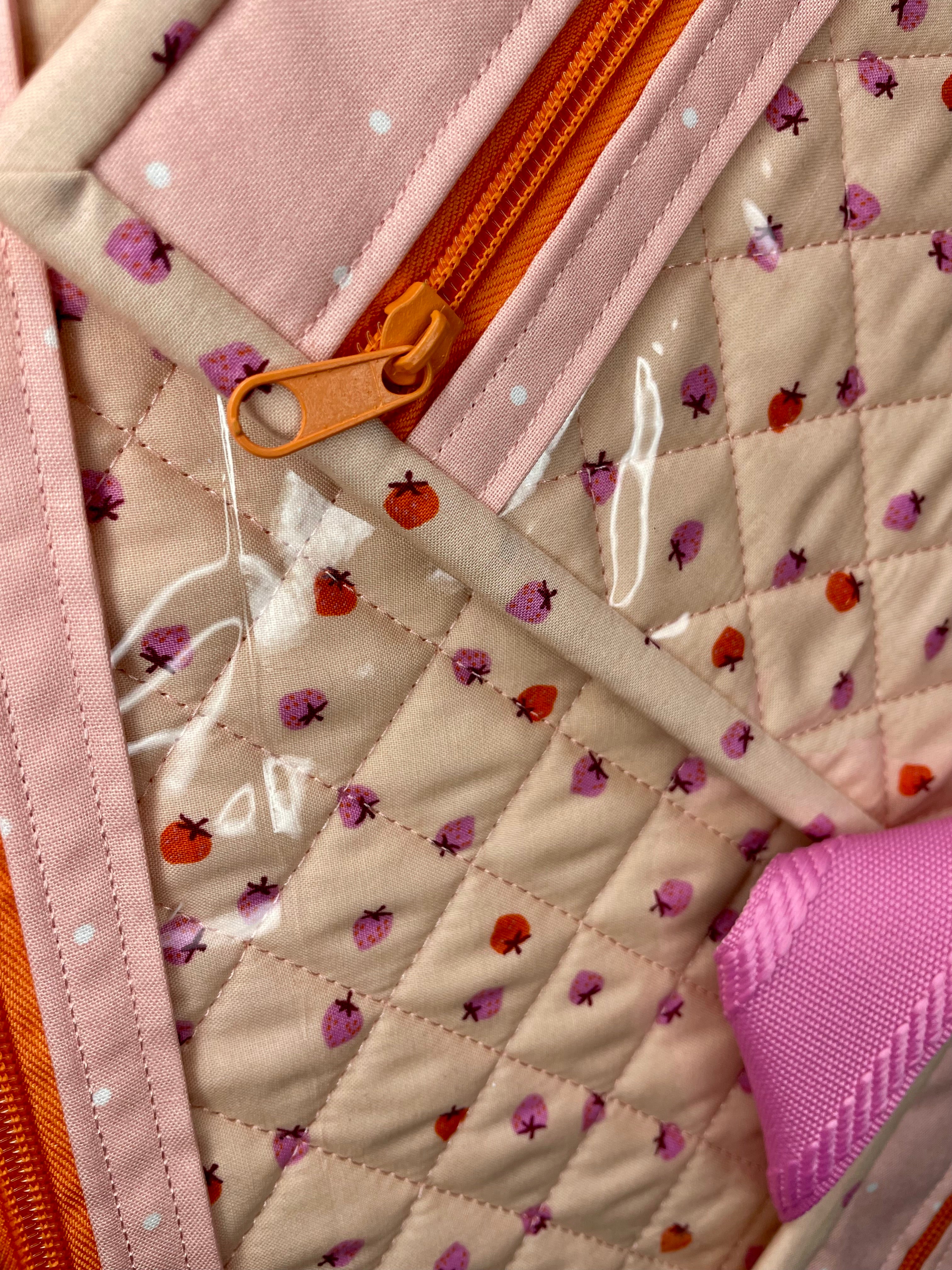 Close-up of a quilted fabric with ladybug pattern and orange zipper.