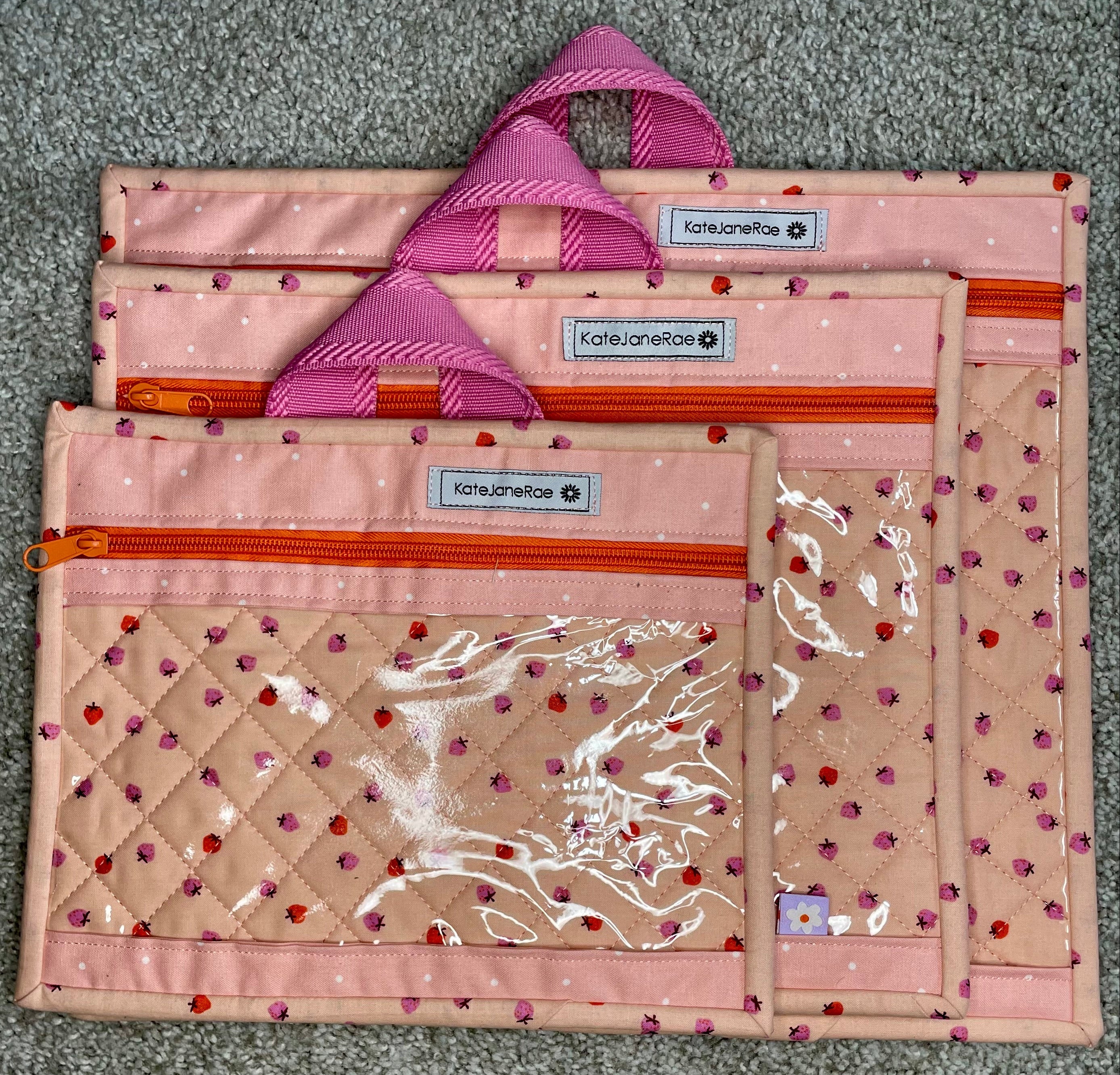 Set of three pink and beige bags with visible branding on a gray surface