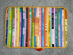 Colorful book-shaped place mat with various book designs on a gray surface