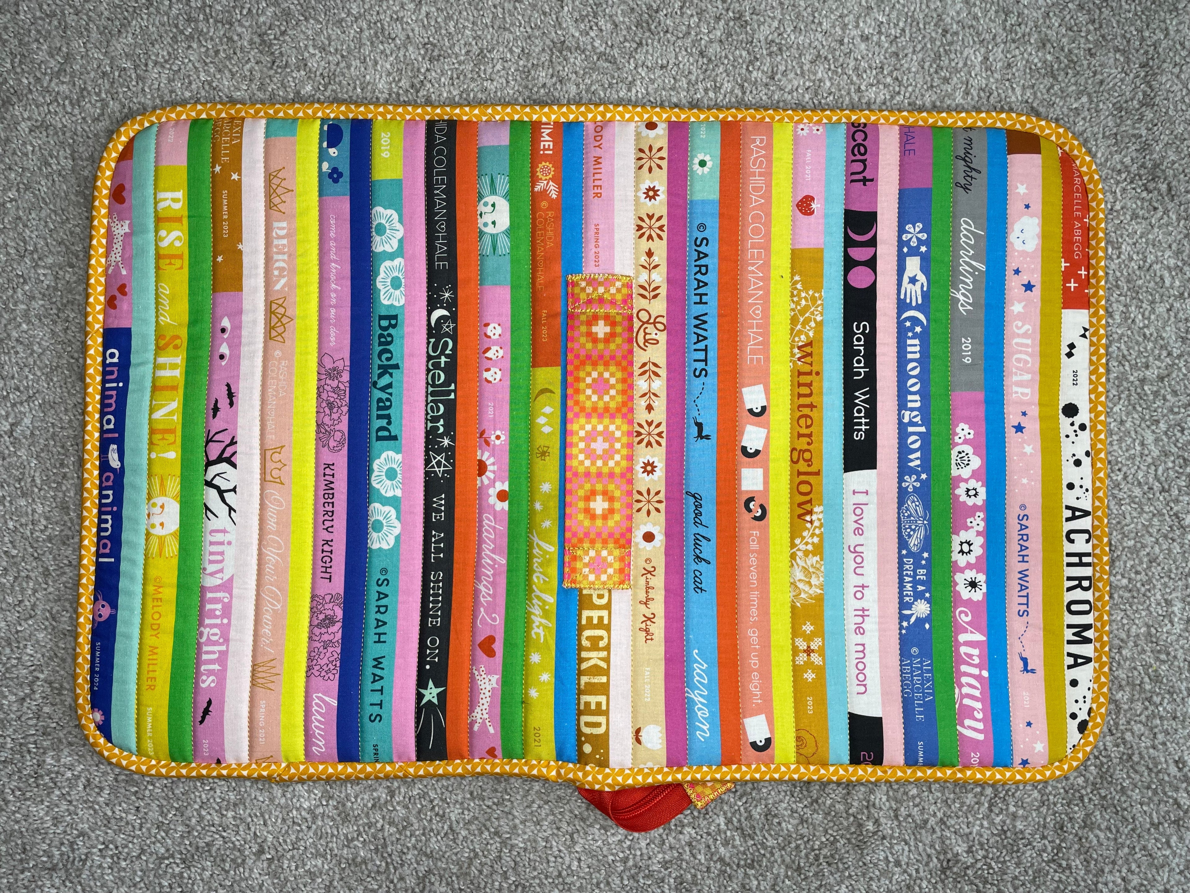 Colorful book-shaped place mat with various book designs on a gray surface