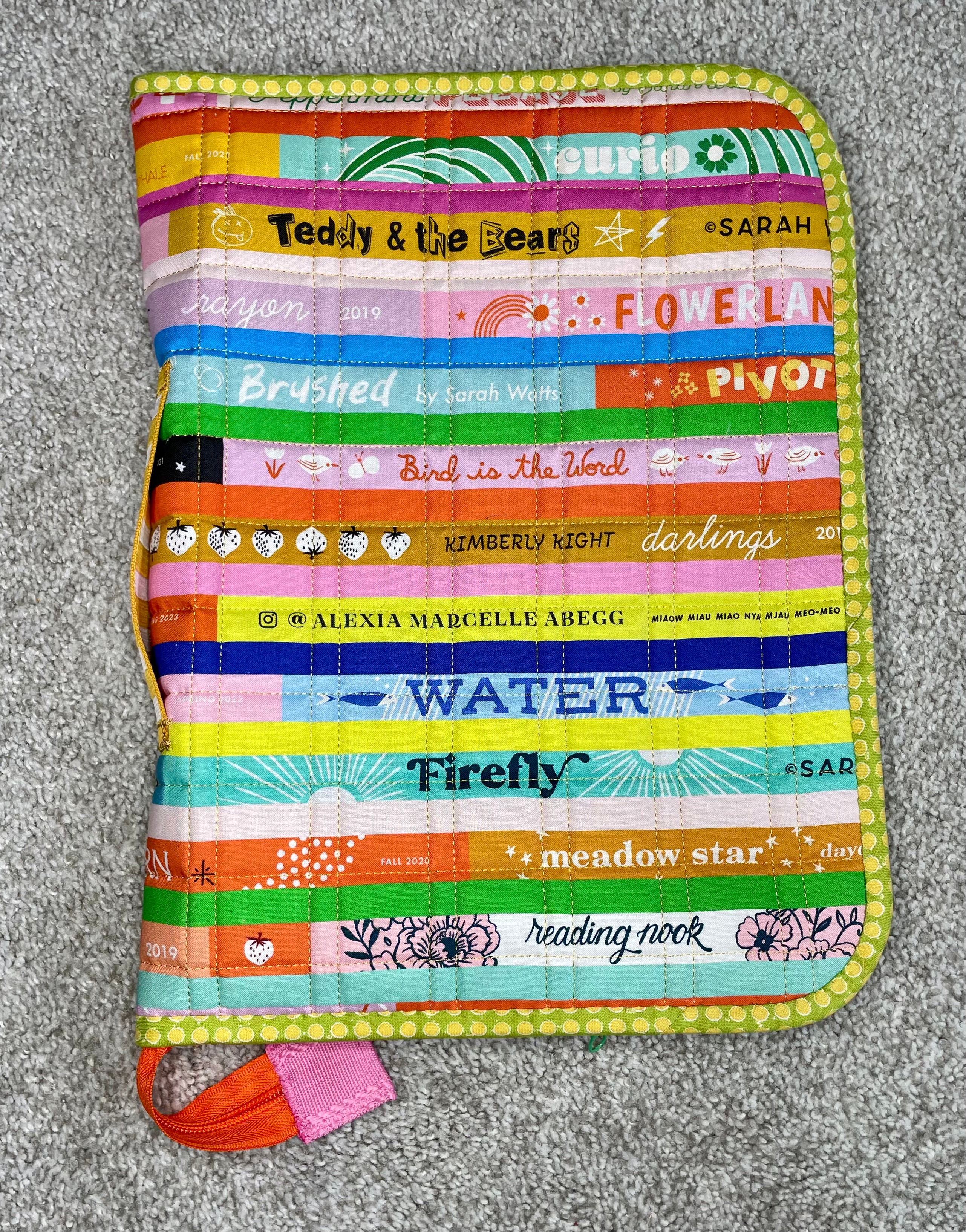 Colorful striped quilt with various text and logos on a gray surface