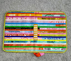 Colorful quilted mat with text and patterns on a gray surface