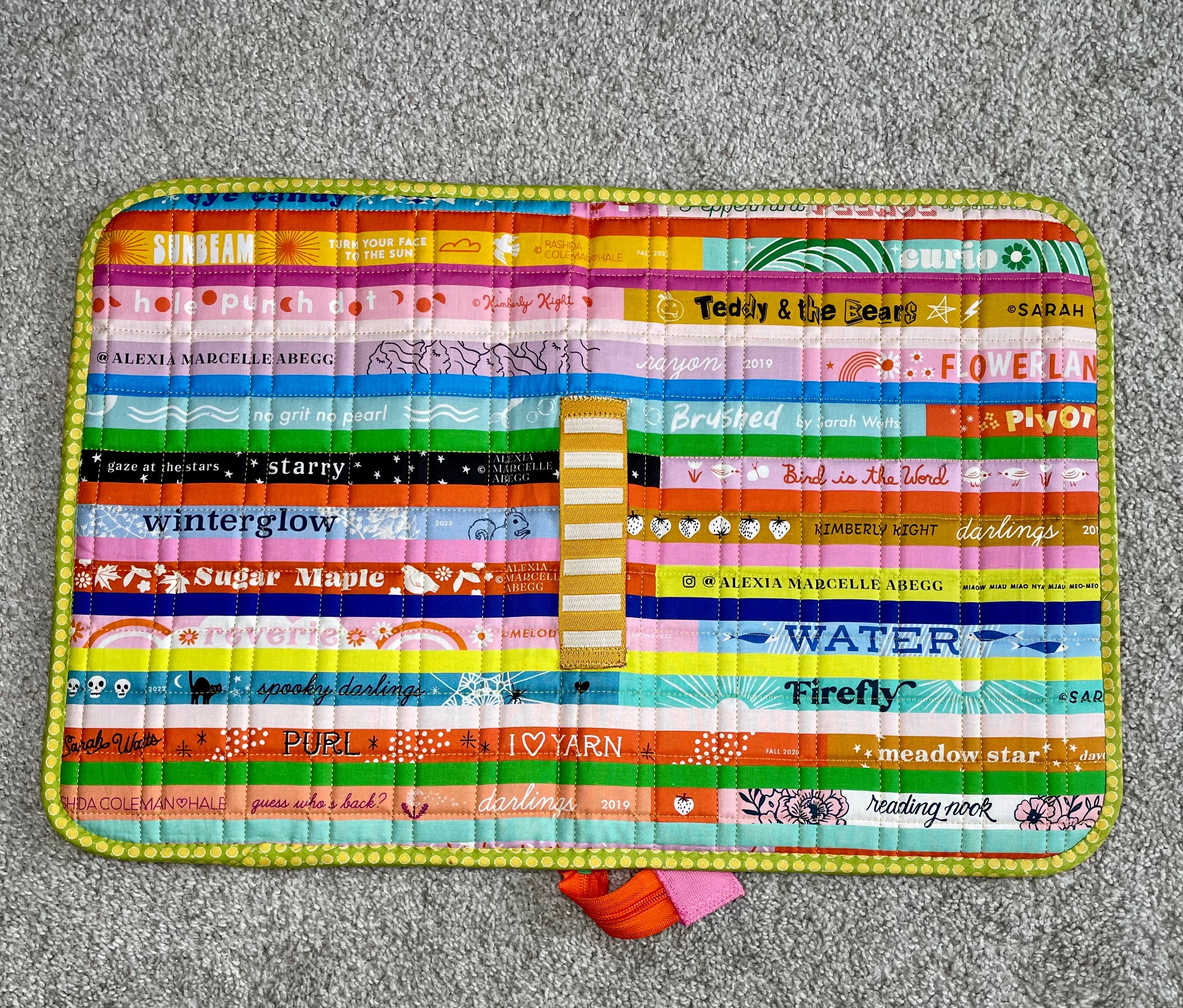Colorful quilted mat with text and patterns on a gray surface