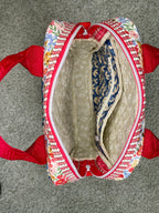 Small bag with colorful pattern and red straps on a gray surface