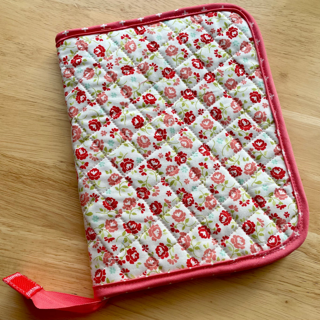 Floral quilted potholder with red border on a wooden surface