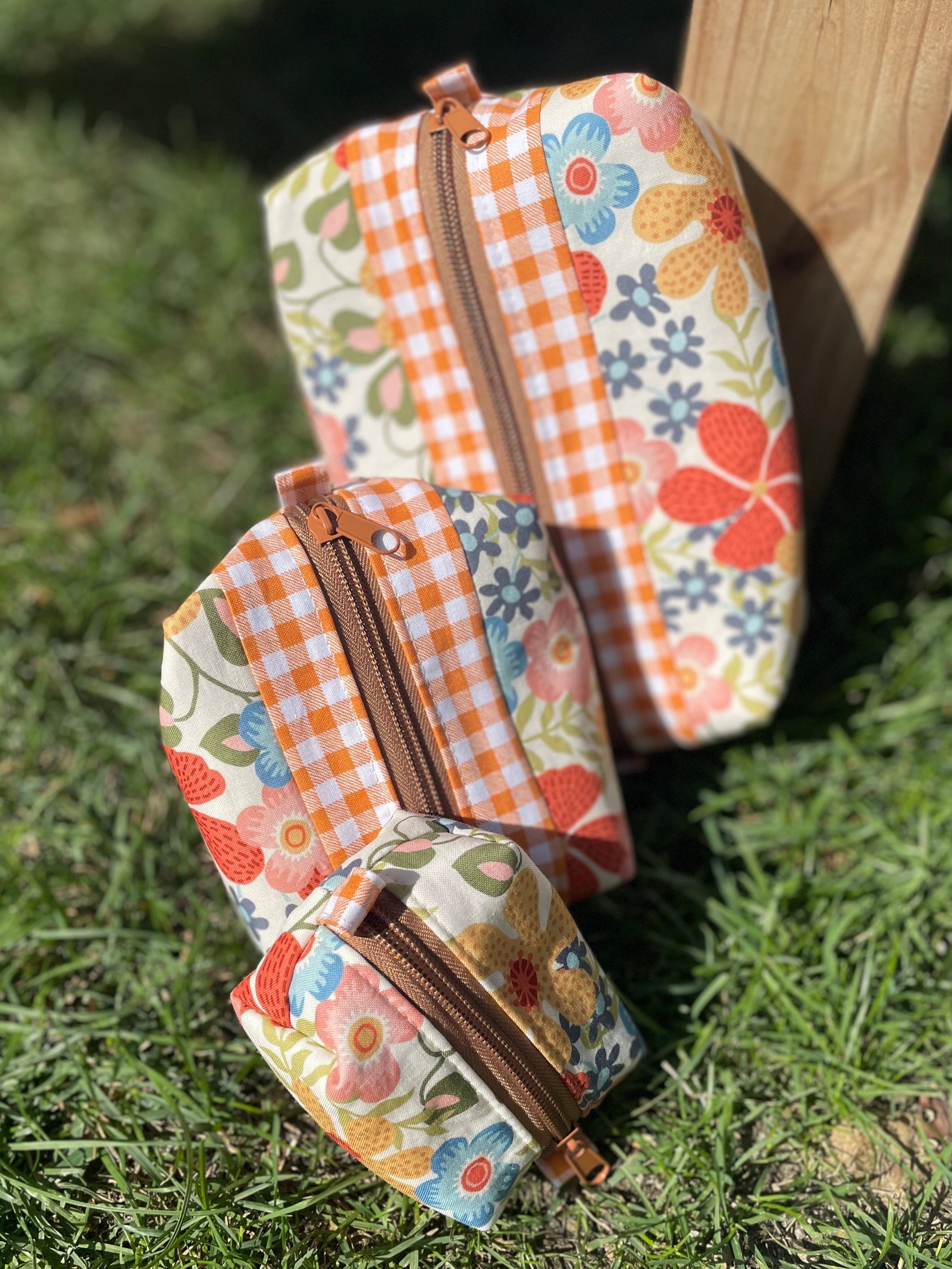 Three fabric pouches with floral and checkered patterns on a grassy background
