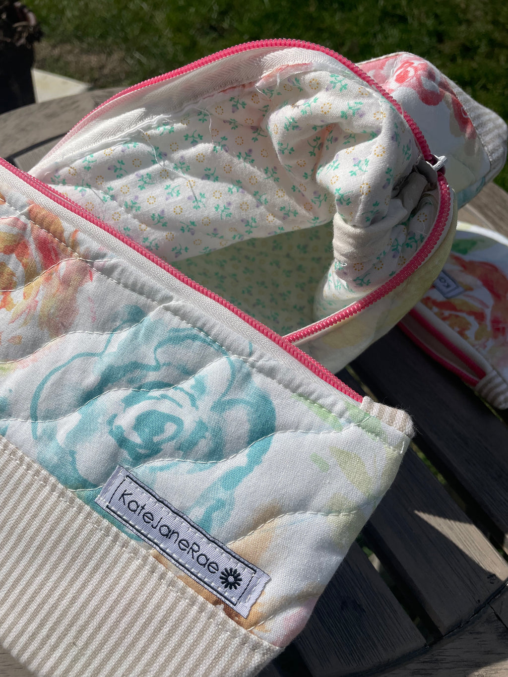 Floral-patterned zipper pouch with a brand label on a wooden surface.