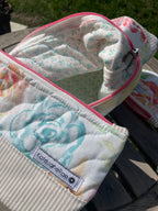 Floral-patterned zipper pouch with a brand label on a wooden surface.