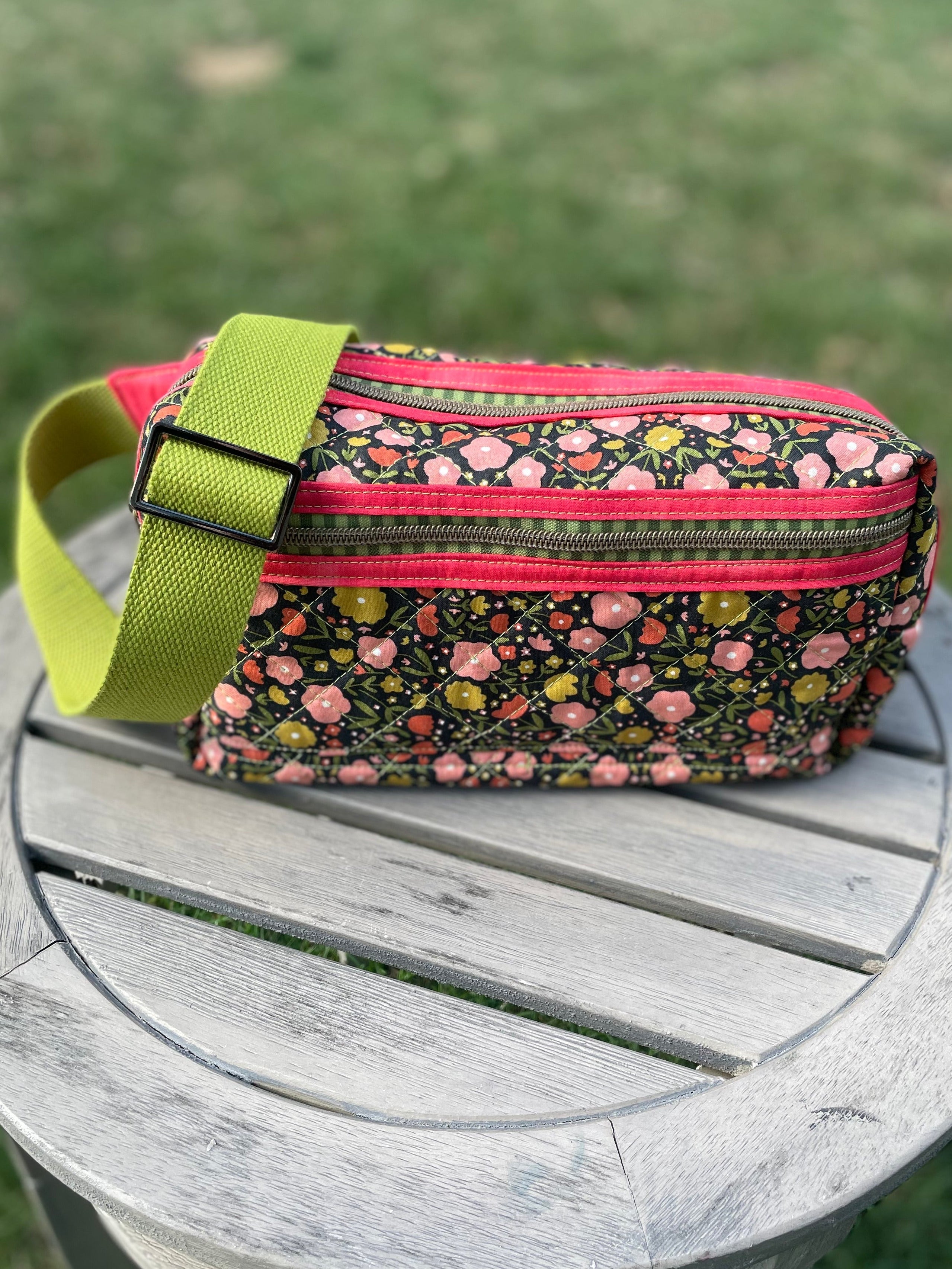 Floral patterned pouch with a green strap on a wooden surface outdoors