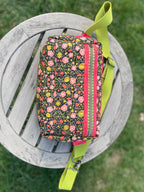 Floral patterned pouch with a green strap on a wooden stool outdoors