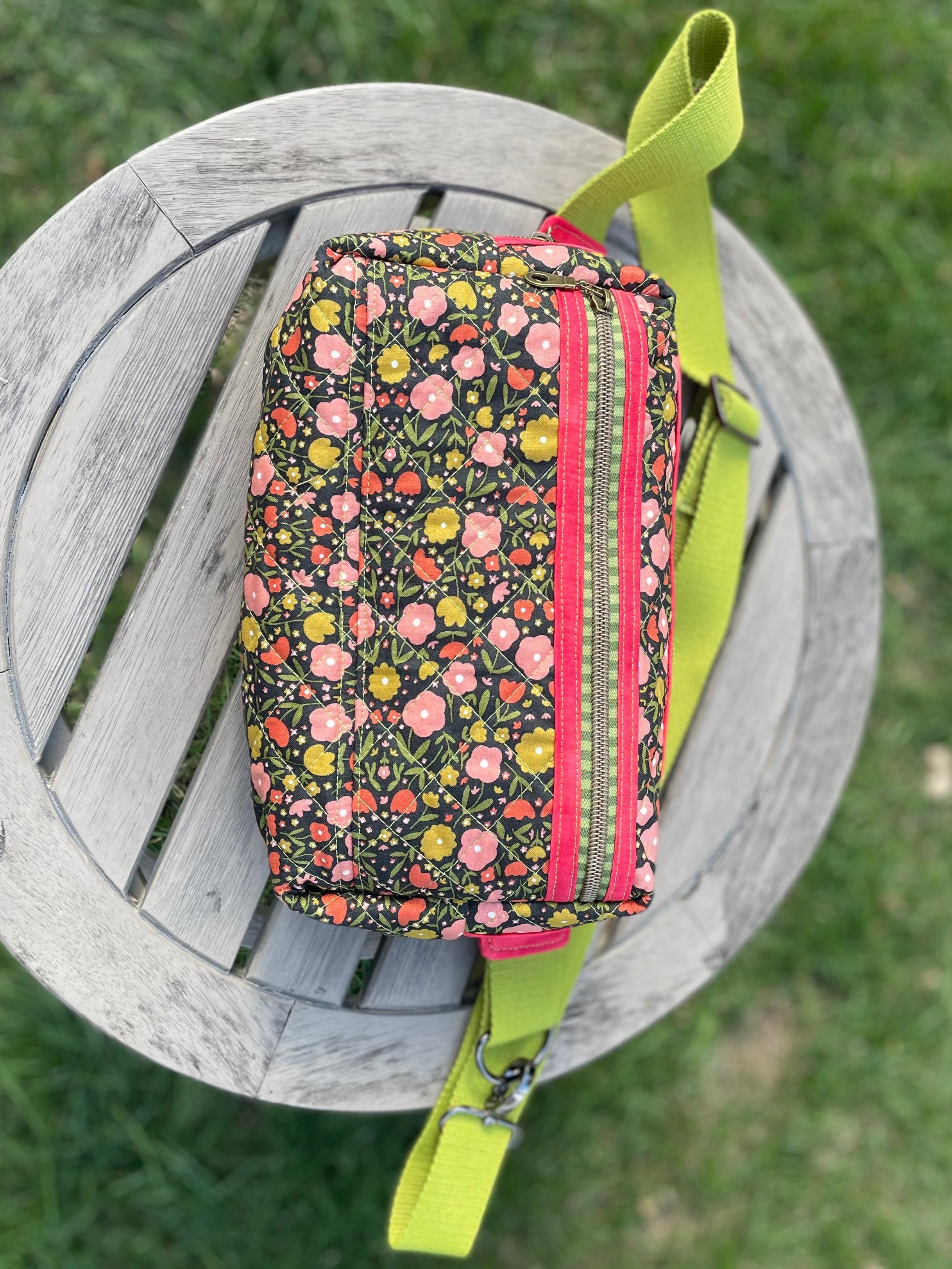 Floral patterned pouch with a green strap on a wooden stool outdoors