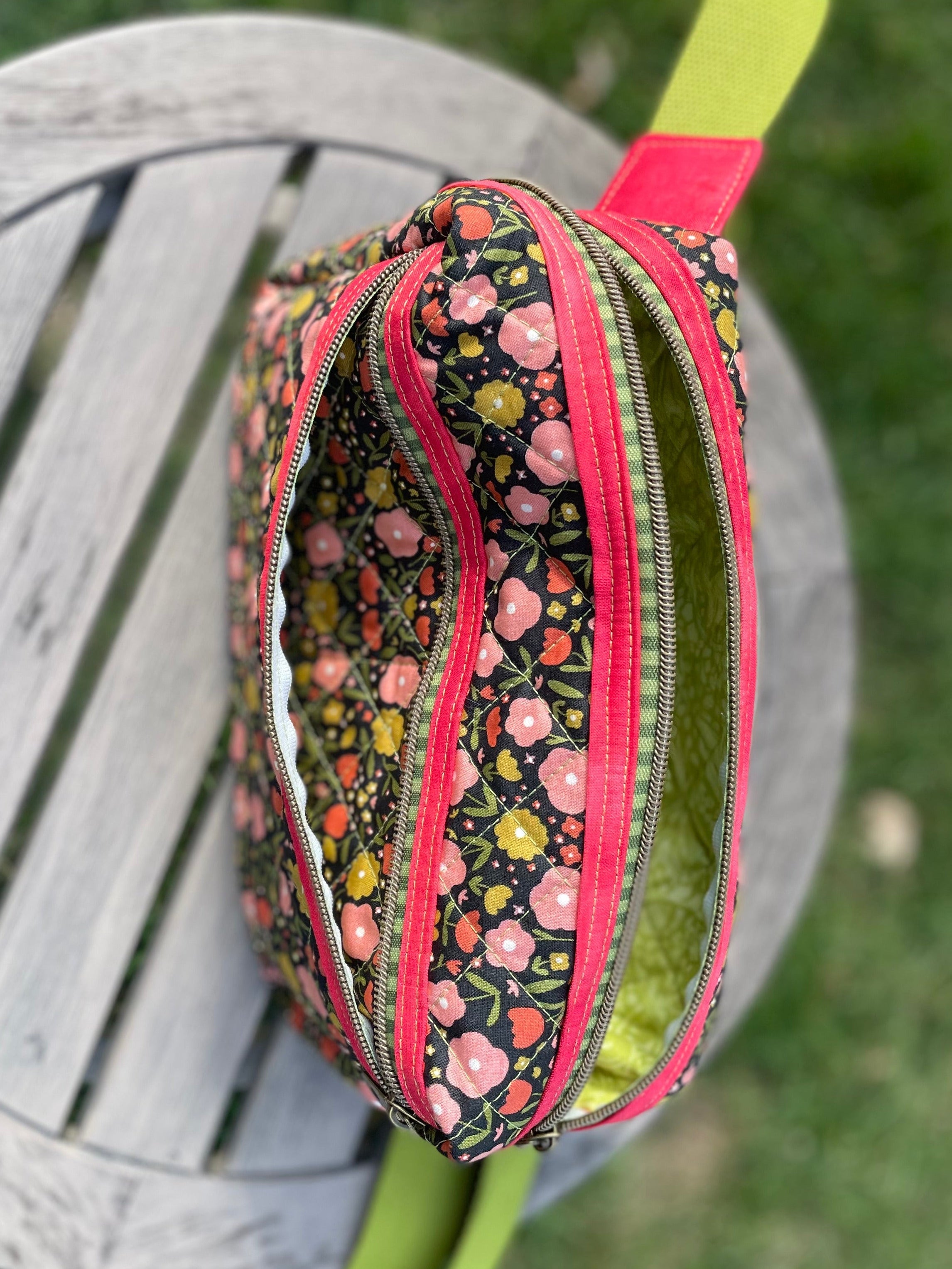 Floral-patterned pouch with a pink zipper on a wooden surface with grass in the background