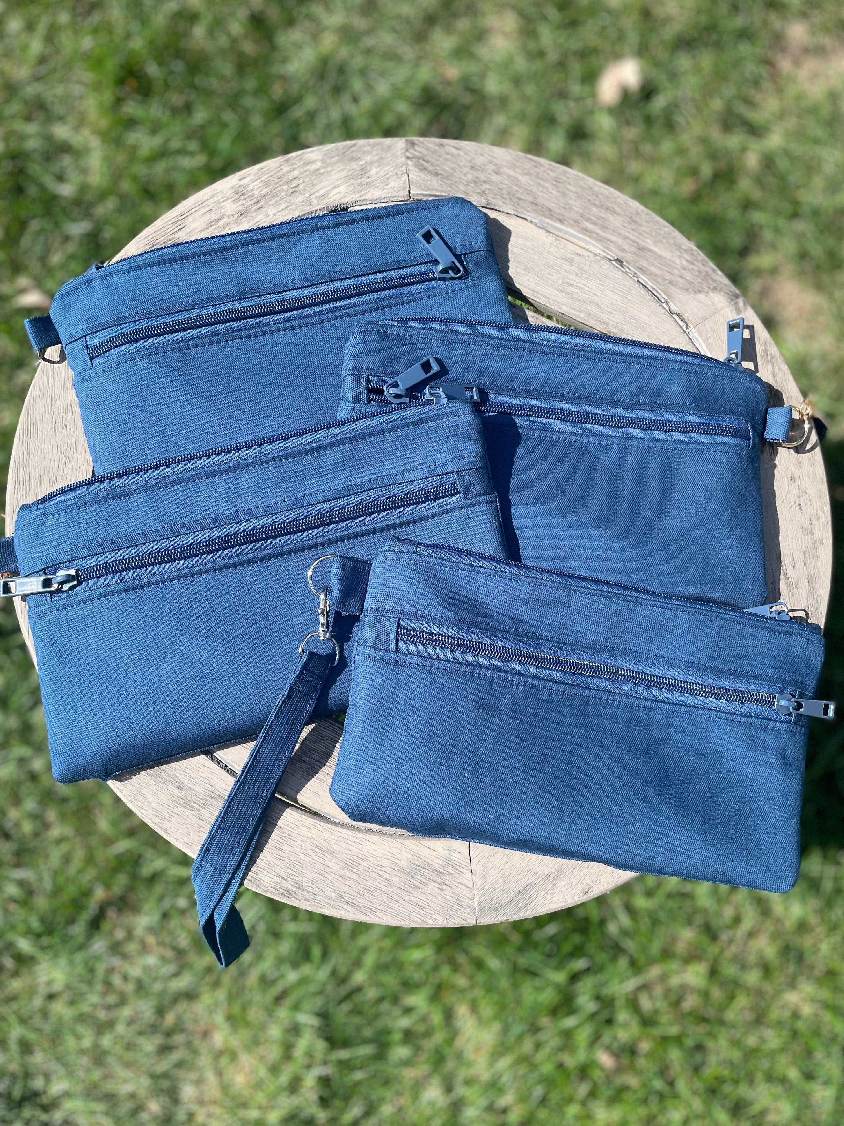 Set of blue bags including a backpack, crossbody bag, and pouch on a wooden surface with grass background.