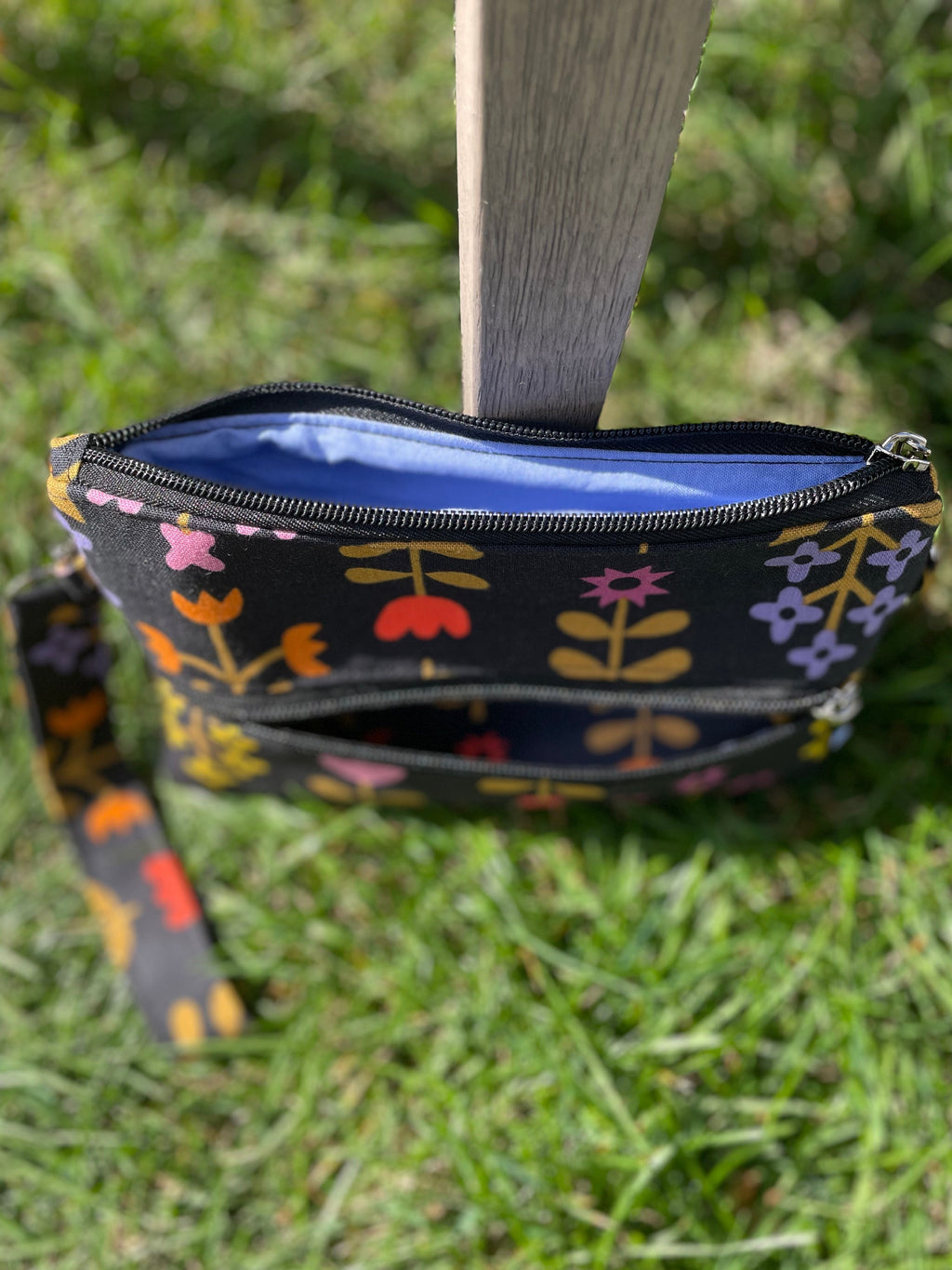 Floral-patterned pouch with a blue interior on a grassy background