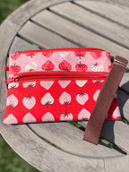 Red pouch with strawberry pattern on a wooden surface outdoors