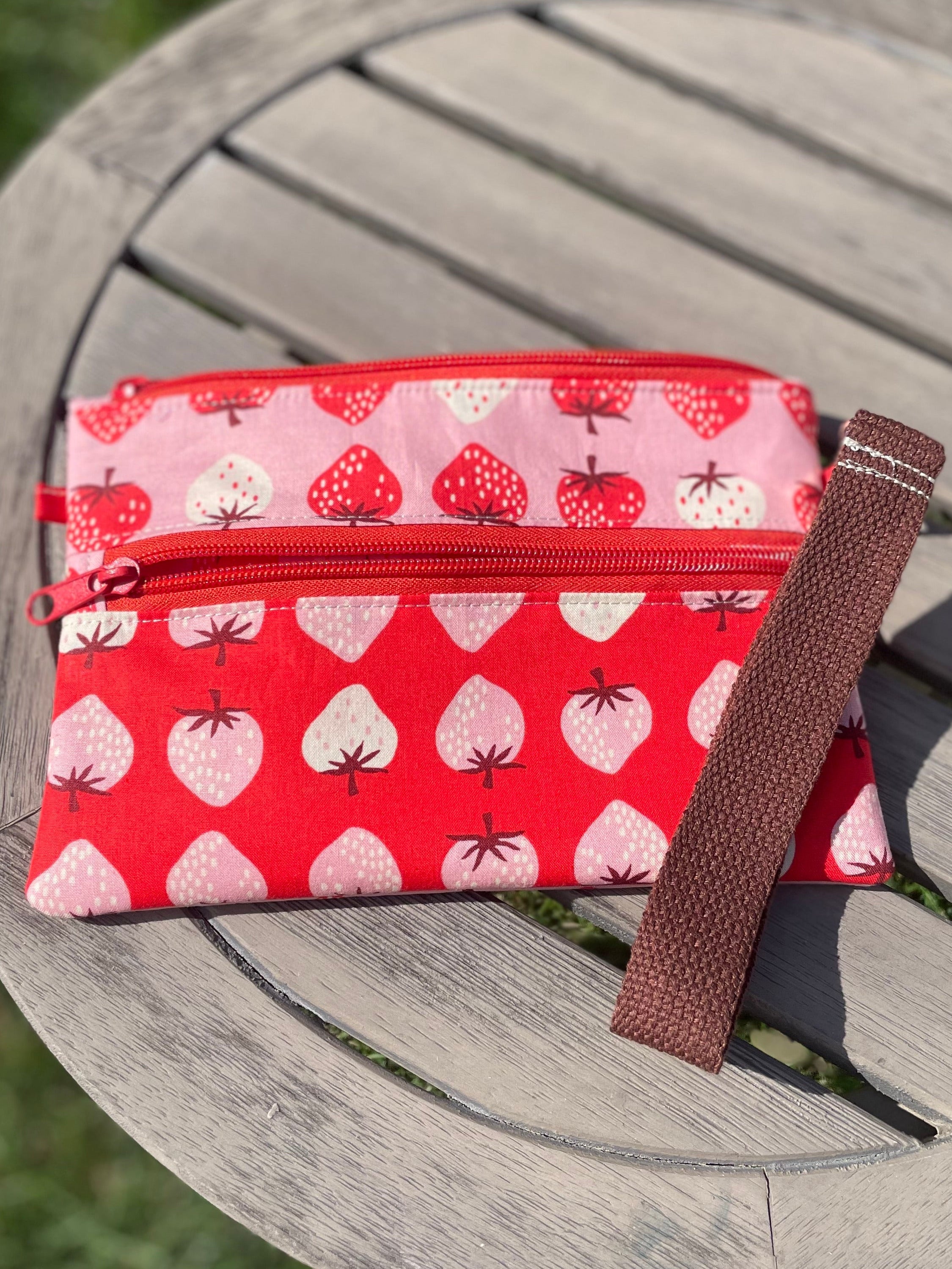 Red pouch with strawberry pattern on a wooden surface outdoors