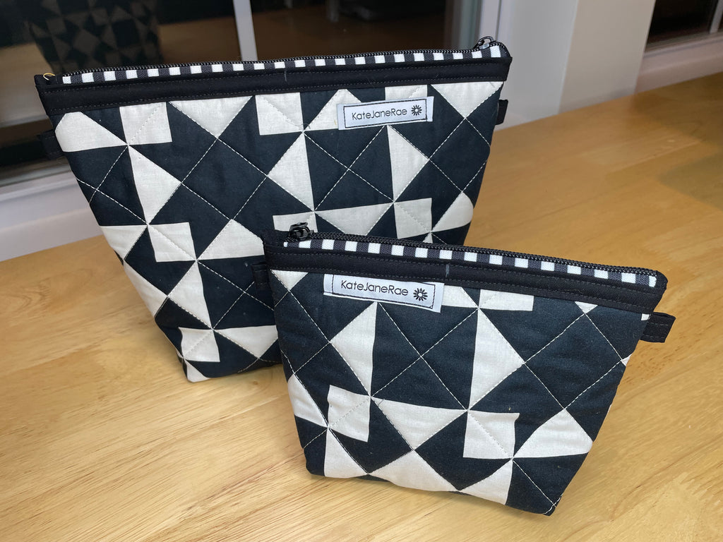 Two quilted zippered pouches with a black and white geometric triangle pattern, displayed on a light wood tabletop. The brand name 'katejaneRose' is visible on the labels.
