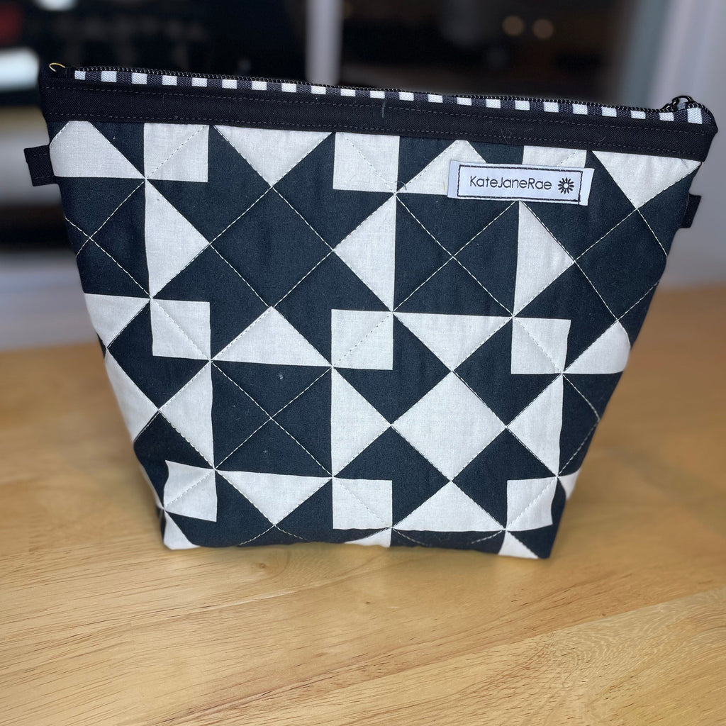 A black and white geometric patterned zippered pouch with a small 'koreapetco' label, sitting on a light wood tabletop.
