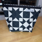 A black and white geometric patterned zippered pouch with a small 'koreapetco' label, sitting on a light wood tabletop.